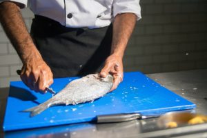 A professional chef Cleaning a Raw Fish on a plastic Cutting Board